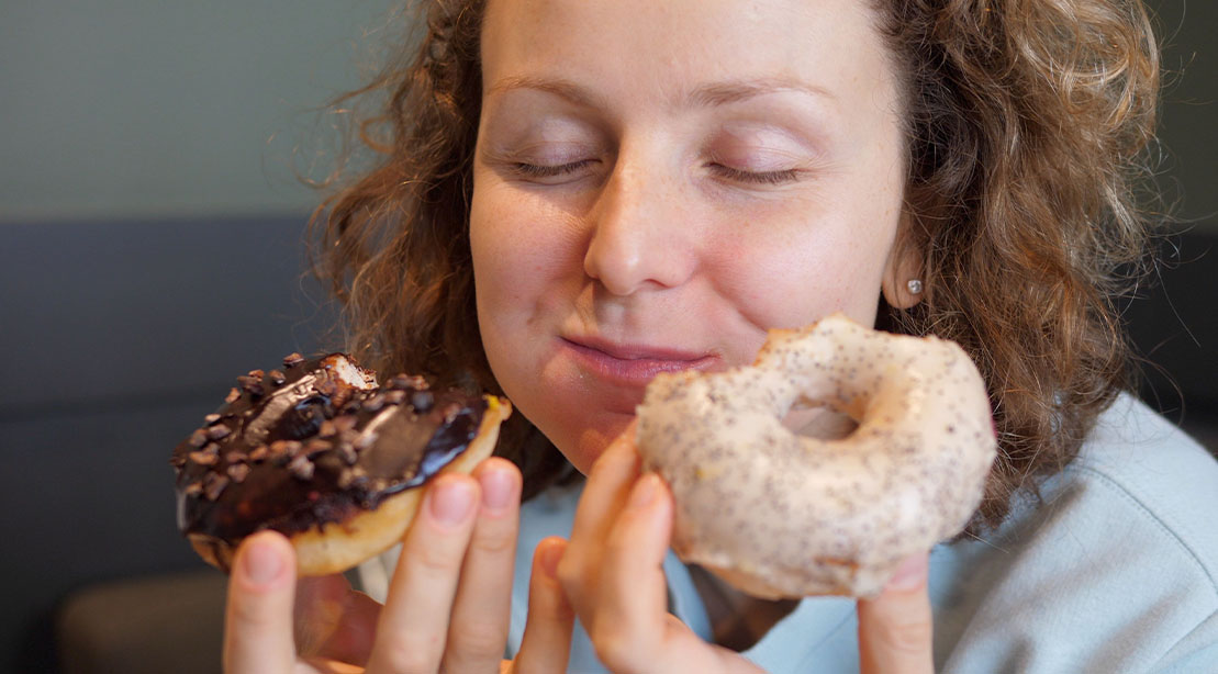 Female with curly hair enjoying eating donuts two at a time
