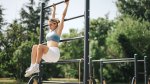 Fit female working out outdoors using hanging knee raises exercise to build her abs