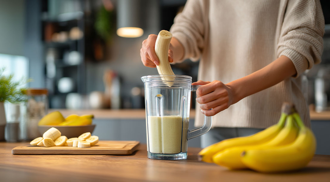 Person putting a banana into a blender to make a banana smoothie